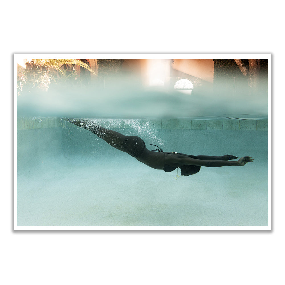 A person in a custom-made black swimsuit gracefully swims underwater in a pool, with sunlight filtering through the blurred poolside view, capturing an image worthy of Francesca Owen's Elegance #2 fine art paper.