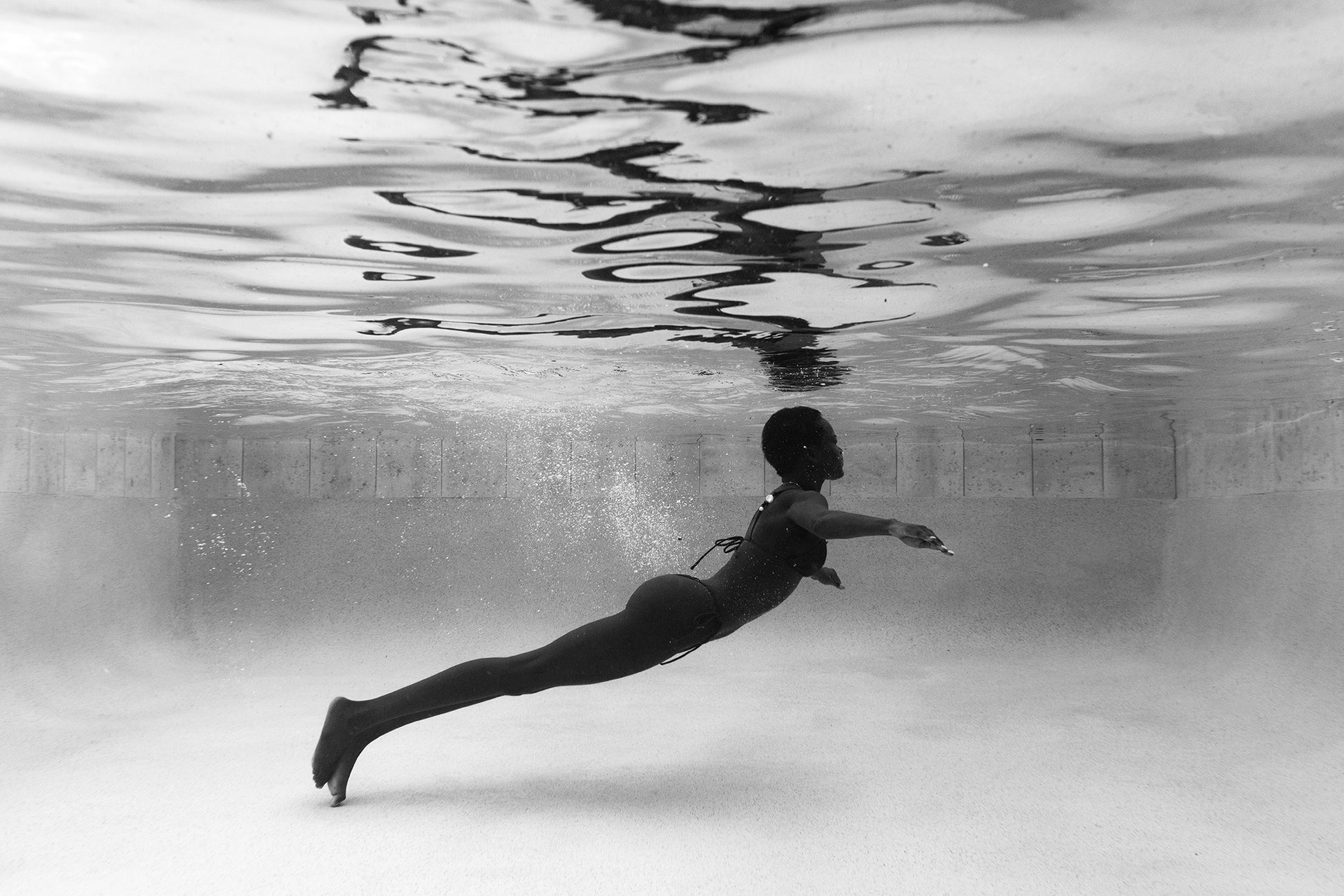 Francesca Owen's Elegance #6 features a black and white underwater image of a person in a horizontal, streamlined pose in a swimsuit, printed on custom-made fine art paper. Ripples dance across the pool's surface.