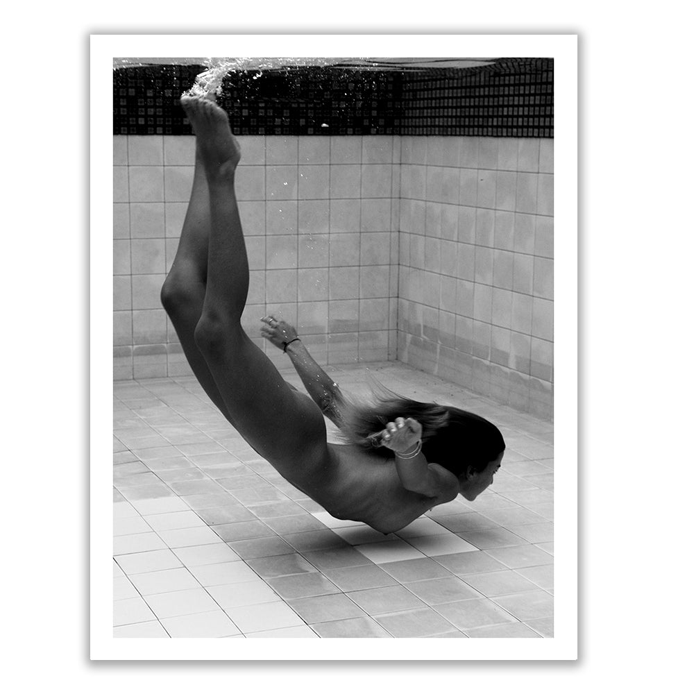 The artwork titled "Fall" by Francesca Owen features a black and white image of a person underwater in a swimming pool. Captured in a horizontal position with legs bent and arms reaching back, the scene is complemented by the surrounding pool tiles visible in the background. This captivating piece is ideal for art prints on fine art paper and custom framing, making it a refined addition to any space.