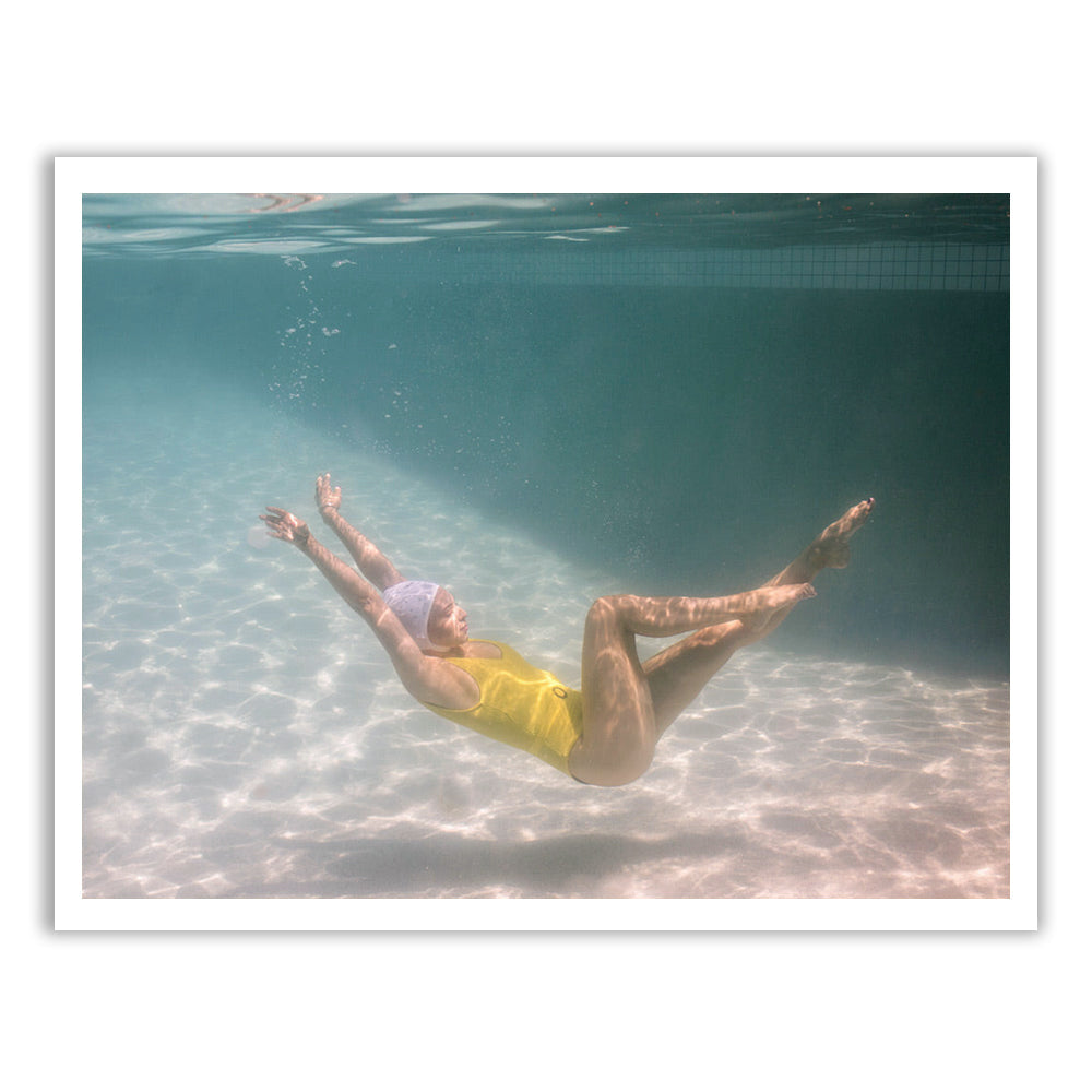 A person in a yellow swimsuit and swim cap is submerged underwater, appearing to be in mid-movement with arms outstretched and legs bent at the knees. Sunlight filters through the water, creating a serene and delicate scene captured on fine art paper using archival pigments. This exquisite artwork, titled Halcyon Daze 1 by Francesca Owen, comes complete with a certificate of authenticity.