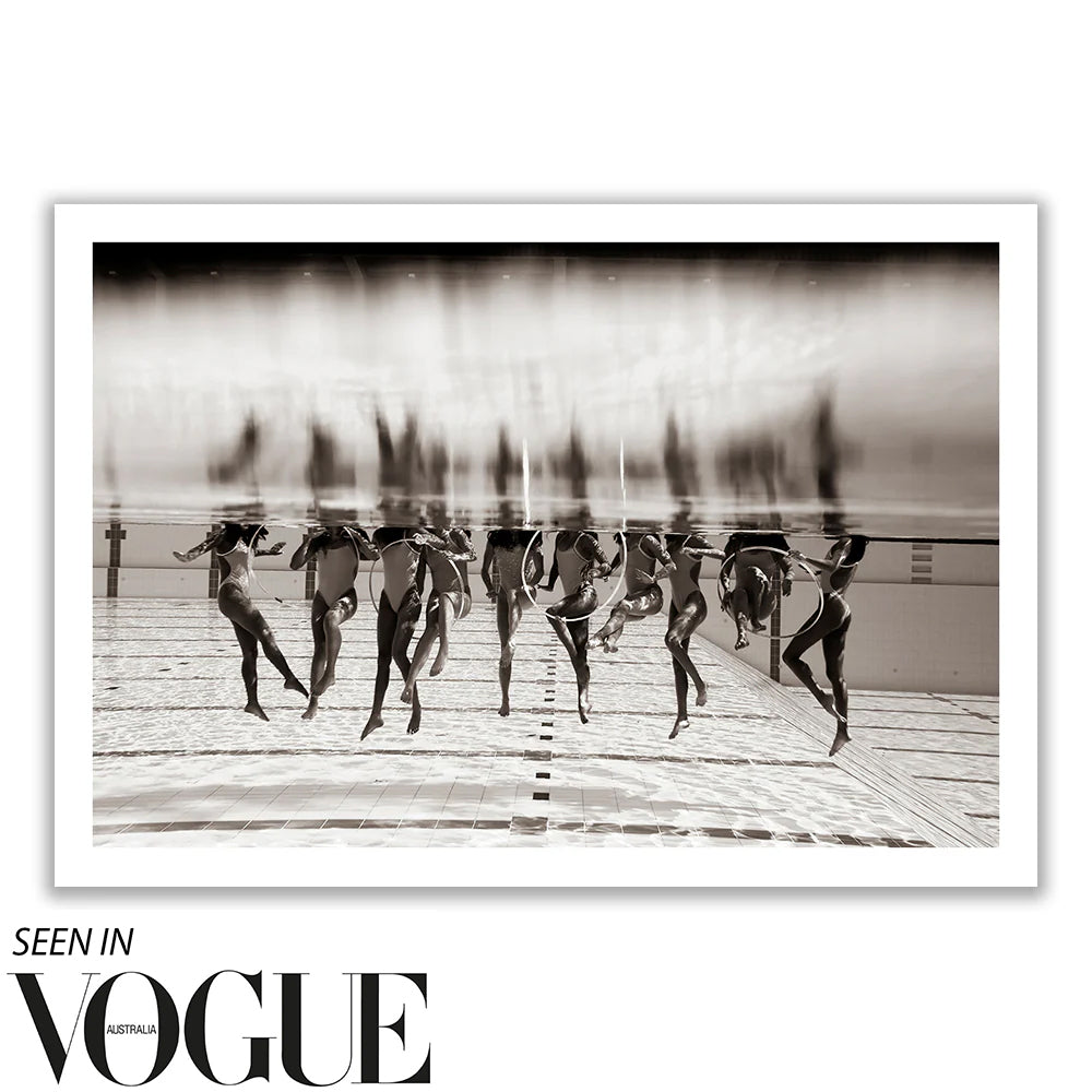 The artwork "Ladies in Waiting #3" by Francesca Owen features a black and white photograph of synchronized swimmers underwater in a pool, showcasing their elegantly extended limbs. This fine art piece highlights the swimmers' grace and coordination and is printed on limited edition giclee fine art paper. A note in the corner reads "Seen in Vogue Australia.