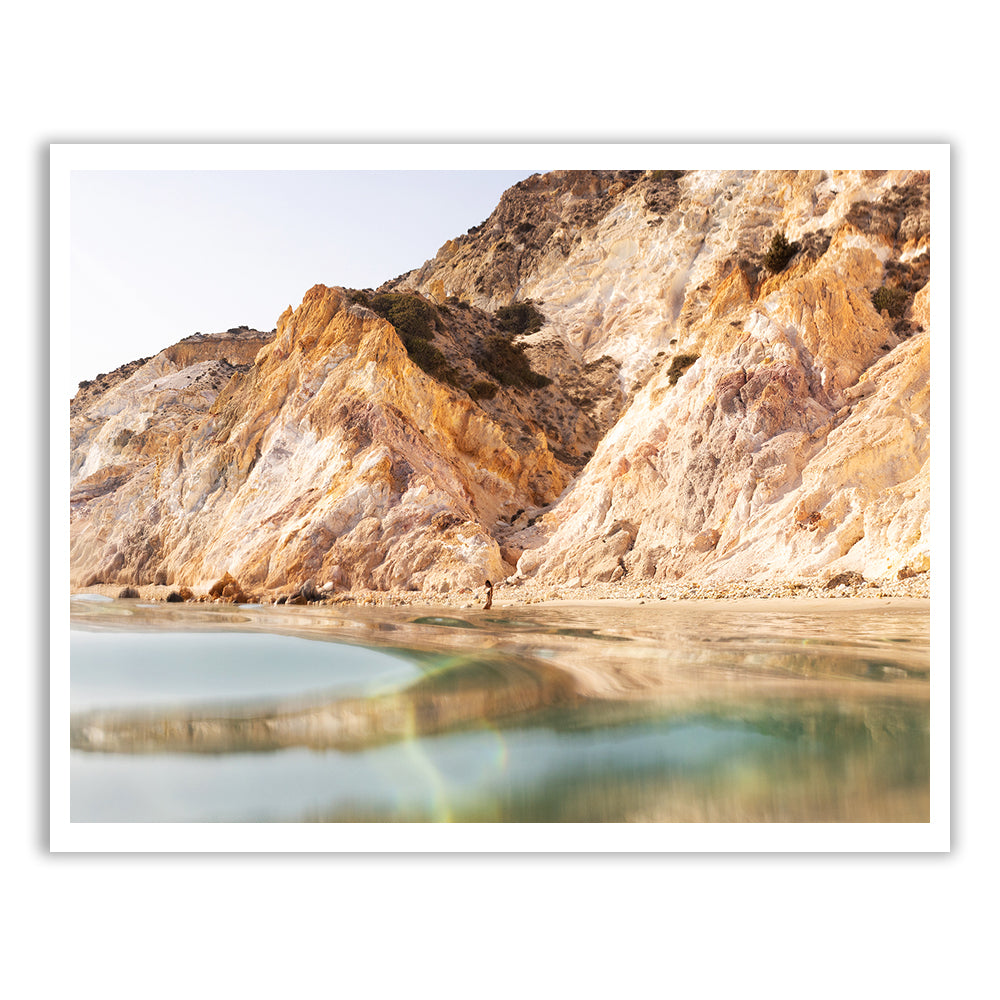 Magic in Milos #9" by Francesca Owen captures a serene landscape of rugged, golden cliffs reflecting in a calm, shallow body of water under a clear sky, using archival pigments on fine art paper.