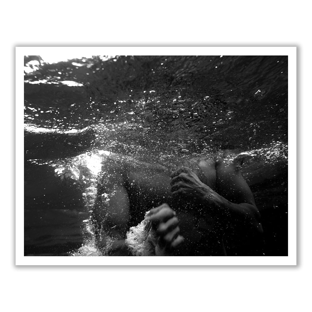 New Waters #3 by Francesca Owen is a black and white photograph showcasing a person partially submerged in water. The image artistically captures the upper body and arm of the individual through the ripples and bubbles on the water's surface, with light reflections creating a dramatic, abstract effect. Available as fine art prints utilizing archival pigments, includes worldwide shipping.