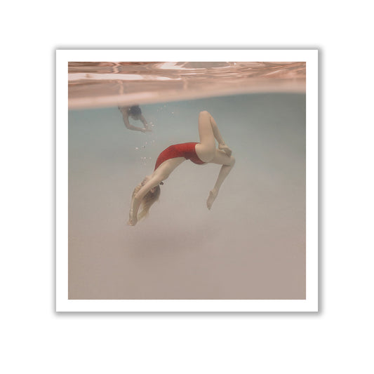 The underwater photograph, titled "Opposites Attract #1" by Francesca Owen, depicts a person in a red swimsuit gracefully arching their body backward. Another individual is also visible in the clear water, with light ripples on the surface. This fine art piece is captured using archival pigments to ensure its longevity and vibrancy.