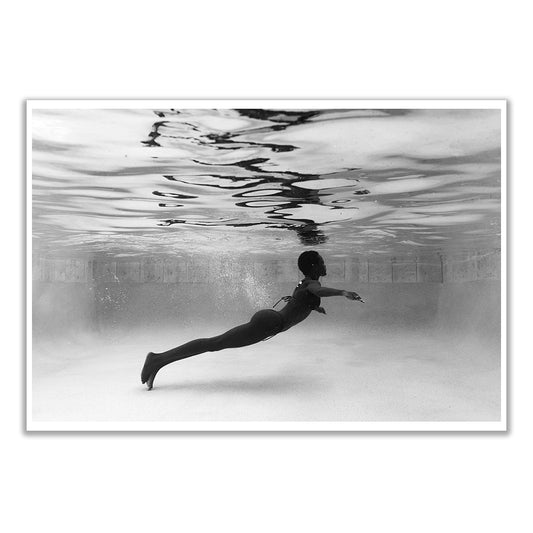 Elegance #6 by Francesca Owen: This archival pigment black and white print on fine art paper depicts a person swimming underwater in a pool, horizontally positioned with arms extended forward, as reflections shimmer above.