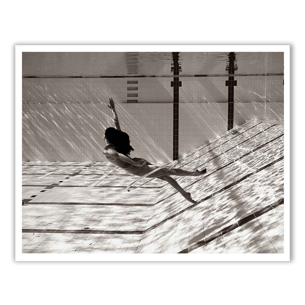 Flying Solo 08," by Francesca Owen, depicts a sepia-toned image of a woman suspended in a diagonally oriented pool beneath calm water. Dressed in a light-colored outfit, she seems to float mid-air with one arm outstretched. The light casts intricate patterns across the pool's tiles, creating a serene atmosphere. This artwork is available as fine art prints featuring archival pigments.