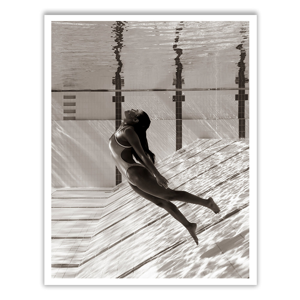 Flying Solo 06" by Francesca Owen is a captivating black-and-white underwater photograph featuring a person with long hair in a swimsuit, gracefully arching backward near the bottom of a swimming pool. Sunlight filters through the water, casting intricate patterns of light and shadows on the pool tiles. This fine art print is produced on archival-quality paper with archival pigments and includes a certificate of authenticity.