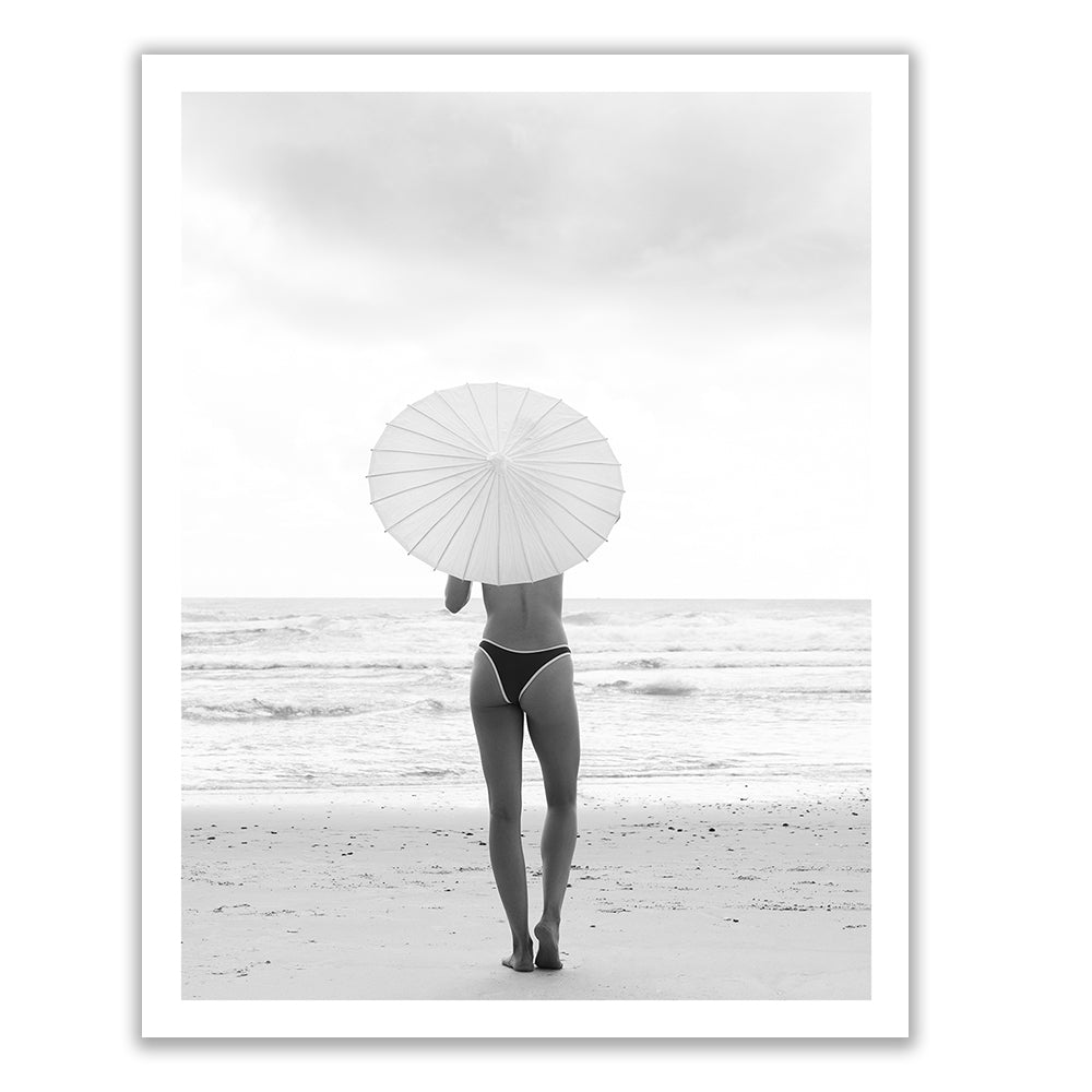 The Beauty Within Part 2 #2" by Francesca Owen features a black and white photo of a person standing on a beach, facing the ocean, holding a large, round umbrella. The person is wearing minimal clothing and the sky appears overcast. This photograph is captured with archival pigments on fine art paper for timeless quality.