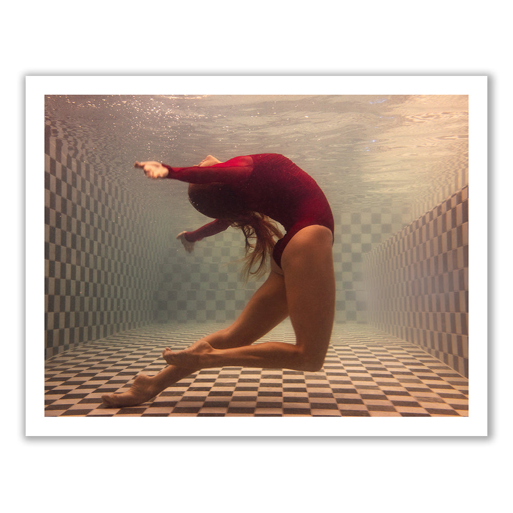 A person in a red swimsuit arches their back gracefully underwater in a checkered-tile swimming pool. Their hair flows freely and their arms extend back, creating a dynamic and fluid pose, reminiscent of the signature style captured by Francesca Owen in her artwork "Wild at Heart no.3.