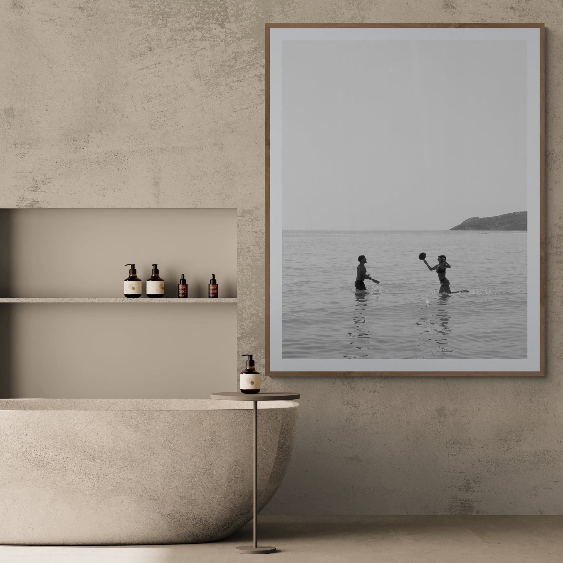 In the minimalist bathroom, a freestanding tub is complemented by a small table holding a bottle and shelves stocked with toiletries. Adding elegance to the textured wall is "Magic in Milos #8," a large framed photo by Francesca Owen, printed on fine art paper using archival pigments, capturing two people playing in the sea.