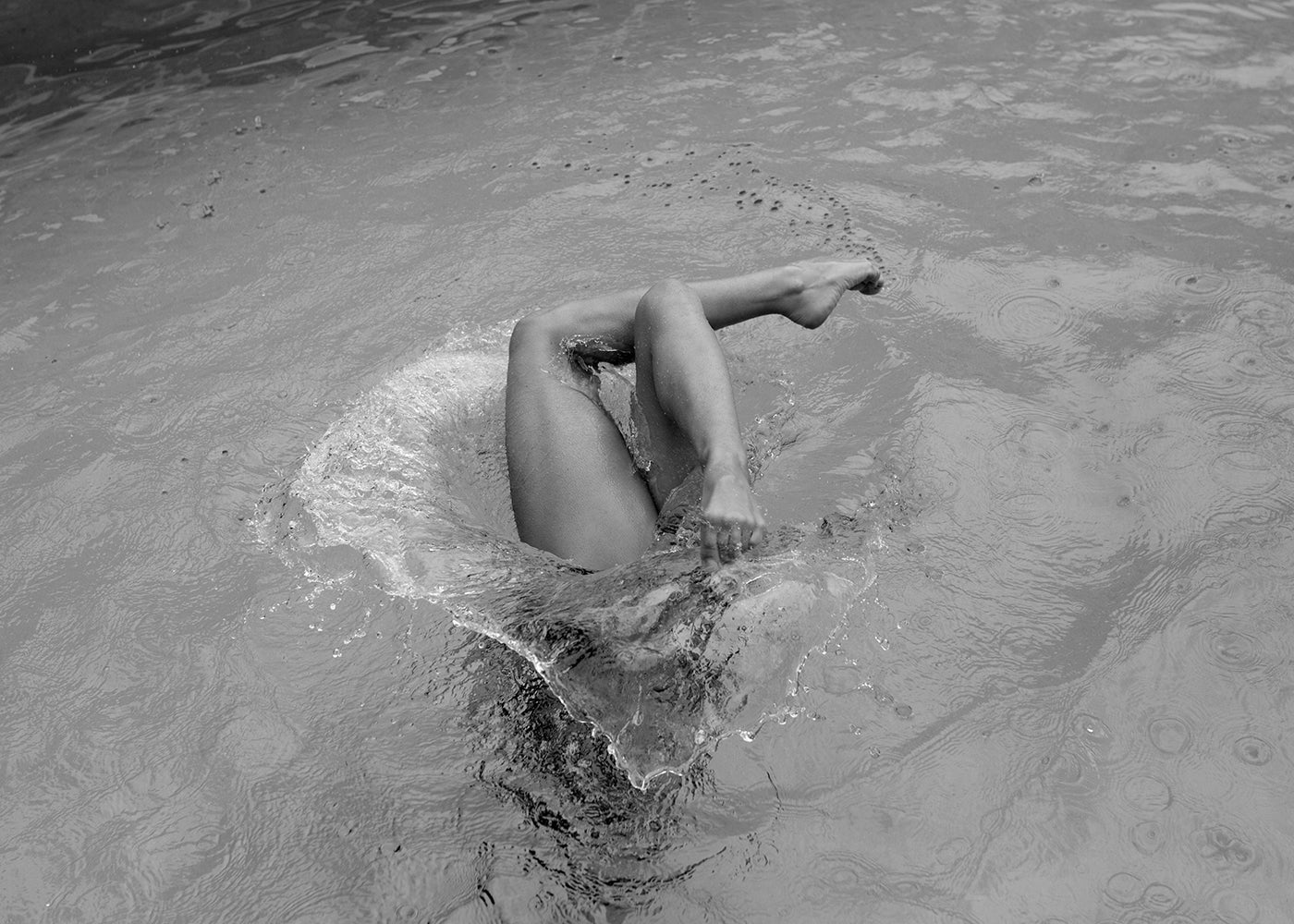 Self Reflection" by Francesca Owen features a black-and-white photo of a person tumbling into water, with legs emerging from the surface and creating a splash. The water, captured in archival pigments, displays ripples and droplets that suggest recent rain or motion. This piece is available as fine art prints, each accompanied by a certificate of authenticity.